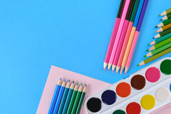 Back to school concept. School equipment with colored pencils and watercolor on blue background. Flat lay, top view, copy space.