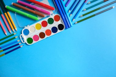 Okul konseptine geri dönelim. Mavi arka plan üzerinde renkli kalemler ve suluboya ile Okul ekipmanları. Düz döşeme, üst görünüm, kopyalama alanı.