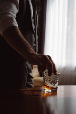 Bir bardak viski tutan insan elinin dikey görüntüsü. Tatma ve degustation kavramı. Bir bardak viski ile şık takım elbiseli işadamı.