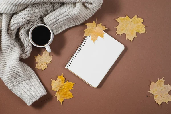 Werkruimte met gouden esdoorn bladeren, notebook, koffie kopje, trui op bruine achtergrond. Creatieve compositie. Herfst-of winter concept. Platte lay, bovenaanzicht — Stockfoto