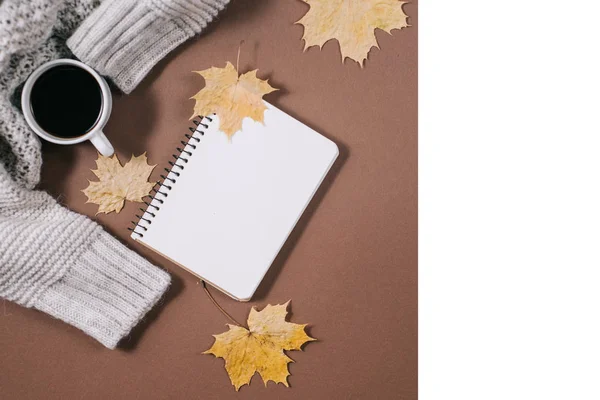 Werkruimte met gouden esdoorn bladeren, notebook, koffie kopje, trui op bruine achtergrond. Creatieve compositie. Herfst-of winter concept. Platte lay, bovenaanzicht — Stockfoto