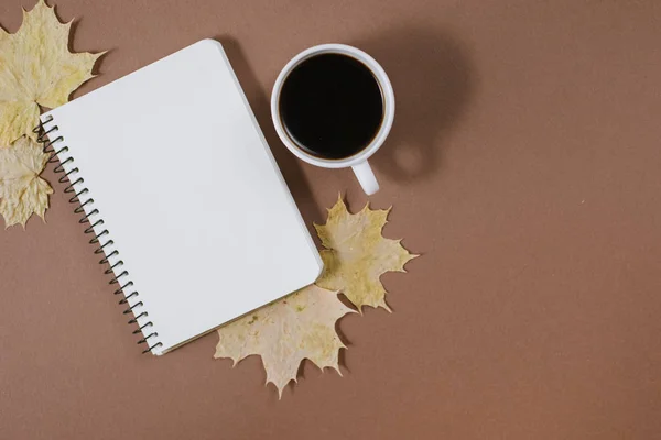 Werkruimte met gouden esdoorn bladeren, hobbels, notebook en kopje koffie op bruine achtergrond. Creatieve compositie. Herfst-of winter concept. Platte lay, bovenaanzicht — Stockfoto