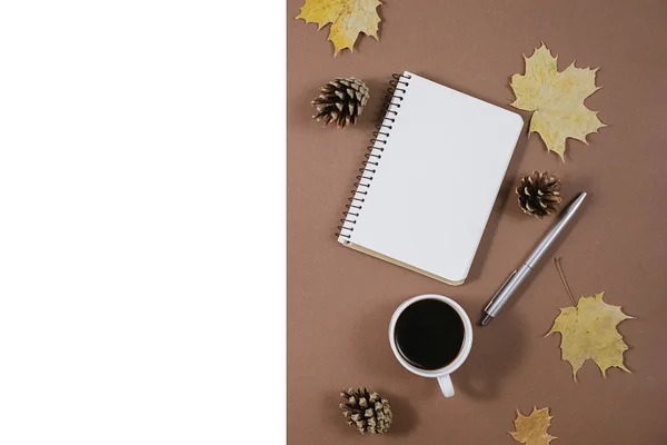 Herfst samenstelling. Gouden esdoorn bladeren, koffie kopje, hobbels, notebook en pen op bruine achtergrond. Herfst-of winter concept. Platte lay, bovenaanzicht — Stockfoto