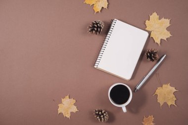 Altın akçaağaç yaprakları, kahve bardağı, darbelere, dizüstü ve kahverengi arka planda kalem ile çalışma alanı. Yaratıcı kompozisyon. Sonbahar veya kış konsepti. Düz yatıyordu, üst görünüm