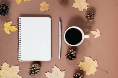 Altın akçaağaç yaprakları, kahve bardağı, darbelere, dizüstü ve kahverengi arka planda kalem ile çalışma alanı. Yaratıcı kompozisyon. Sonbahar veya kış konsepti. Düz yatıyordu, üst görünüm