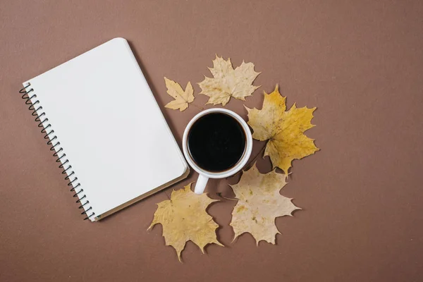 Herfst samenstelling. Kopje koffie, notebook, herfst esdoorn bladeren op bruine achtergrond. Platte lay, bovenaanzicht, kopieer ruimte. — Stockfoto