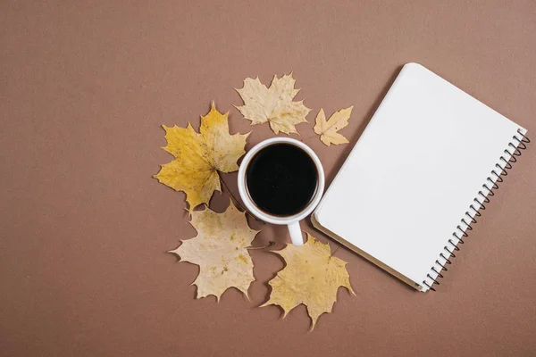 Herfst samenstelling. Kopje koffie, notebook, herfst esdoorn bladeren op bruine achtergrond. Platte lay, bovenaanzicht, kopieer ruimte. — Stockfoto