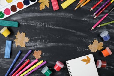 Okul konseptine geri dönelim. Notebook, renkli kalemler, suluboya ve kurutulmuş akçaağaç yaprakları ve ofis malzemeleri siyah masa arka planda. Düz yatıyordu, üst görünüm, kopya alanı.