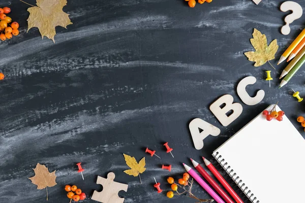 Back to school concept. School equipment with colored pencils, notebook, dried maple leaves and office supplies on black table background. Flat lay, top view, copy space.