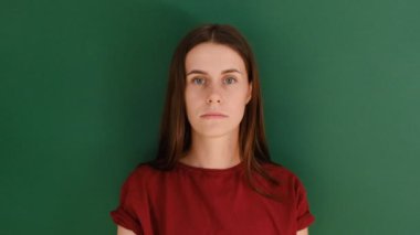 Şaşırmış duygusal kadın elini açık ağzının yanında tutuyor, korkmuş bakıyor, utanmış ve şok olmuş hissediyor, kameraya bakıyor, kırmızı tişört giyiyor, yeşil duvarda izole edilmiş..