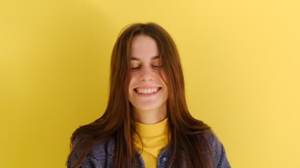 良い若い女の子が喜んで笑いを停止しようとすると 口をカバー笑いながら 黄色の壁に隔離された青いセーターを身に着けているクスクス笑う 人と感情の概念 — ストック動画