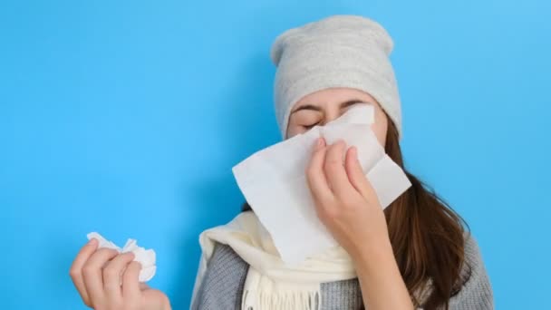 ヘッドギアの病気の白人男性女性 鼻を吹いてインフルエンザにかかった青い背景の組織で冷たいくしゃみを ナプキンを持つ咳をするアレルギー症状を持つアレルギー症状を持つアレルギーの女の子 — ストック動画