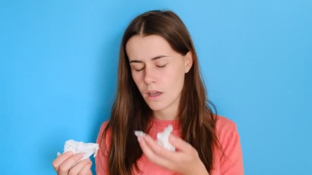 病気の女性の肖像画は 鼻をくしゃみ ハンカチを使用し 感染症を持っているか 何かにアレルギーを持っている カジュアルな服を着て 青い背景の上に隔離されています 病気の概念 — ストック動画