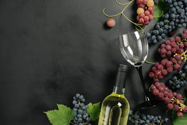 A bottle, wine glasses, fresh grapes and leaves on black background. Flat lay, top view, copy space. Wine bar, winery, wine tasting concept