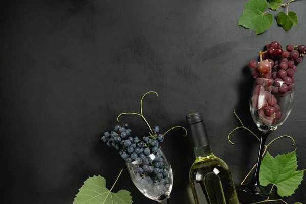 Garrafa, dois copos de vinho, uvas frescas e folhas sobre fundo preto. Deitado plano, vista superior, espaço de cópia. Wine bar, adega, conceito de degustação de vinhos — Fotografia de Stock