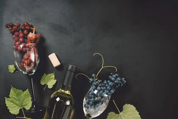 Flat-lay de uma garrafa, dois copos de vinho, uvas frescas e cortiça sobre fundo preto, vista superior, espaço de cópia. Wine bar, adega, conceito de degustação de vinhos — Fotografia de Stock