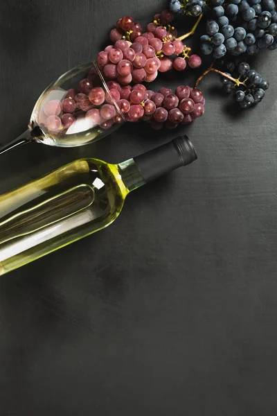 A bottle, wine glasses, fresh grapes on black background. Flat lay, top view, copy space. Wine bar, winery, wine tasting concept