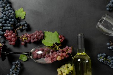 Şişe, iki şarap bardağı, taze üzüm ve siyah arka planda yapraklar. Düz döşeme, üst görünüm, kopyalama alanı. Şarap barı, şaraphane, şarap tatma konsepti