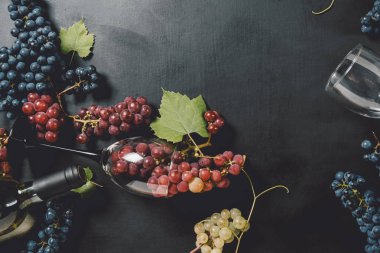 Beyaz şarap şişesi, şarap kadehleri, taze üzüm ve siyah ahşap arka plan üzerinde yaprakları. Düz döşeme, üst görünüm, kopyalama alanı. Şarap barı, şaraphane, şarap tatma konsepti