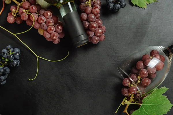 Uma garrafa, copos de vinho, uvas frescas e folhas sobre fundo preto. Deitado plano, vista superior, espaço de cópia. Wine bar, adega, conceito de degustação de vinhos — Fotografia de Stock
