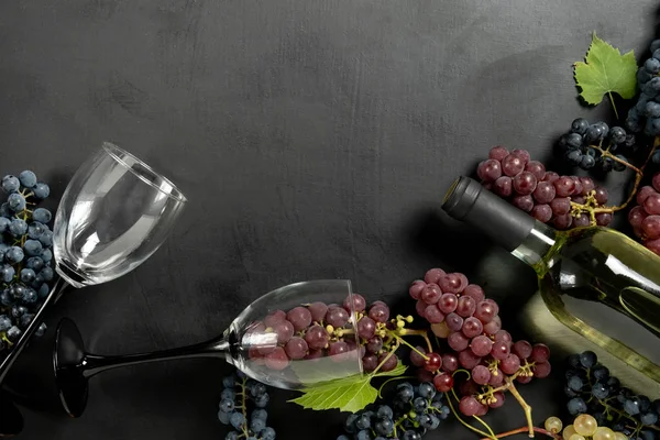 Garrafa, dois copos de vinho, uvas frescas e folhas sobre fundo preto. Deitado plano, vista superior, espaço de cópia. Wine bar, adega, conceito de degustação de vinhos — Fotografia de Stock