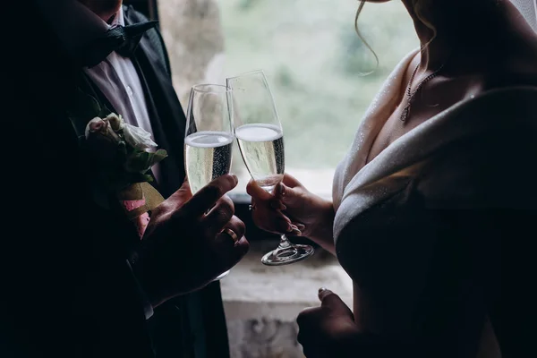 Close up of silhouette married couple toasting champagne glasses at wedding party. Hands bride and groom clinking glasses at wedding reception.