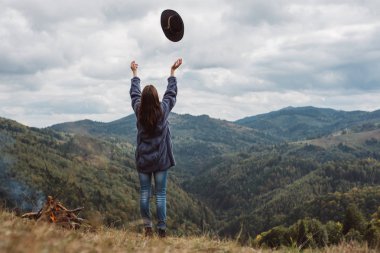 Güzel şık kız Açık yatay görüntü alan boyunca yürür ve şapkasını atar. Genç kadın maceraperest veya turist sonbahar dağlarına bakan bir uçurumun kenarında dayanıyor