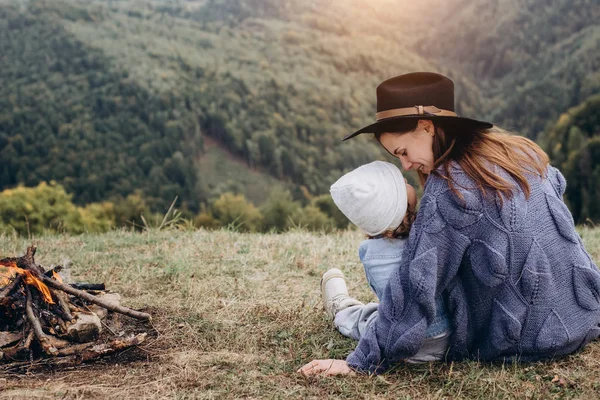Μια νεαρή μητέρα και η όμορφη κόρη της κάθονται κοντά στη φωτιά σε βουνά σε άγριο Εθνικό Πάρκο δάσος. Η οικογένεια των ταξιδευτής χαλαρώνει μετά την ορειβασία. Καυκάσια γυναίκα με μωρό στα βουνά — Φωτογραφία Αρχείου