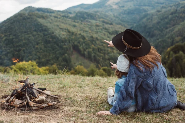 Όμορφη νεαρή μητέρα παίζει με την κόρη κοντά στη φωτιά σε βουνά σε άγριο Εθνικό Πάρκο δάσος. Η οικογένεια των ταξιδευτής χαλαρώνει μετά την ορειβασία. Καυκάσια γυναίκα με μωρό στα βουνά — Φωτογραφία Αρχείου