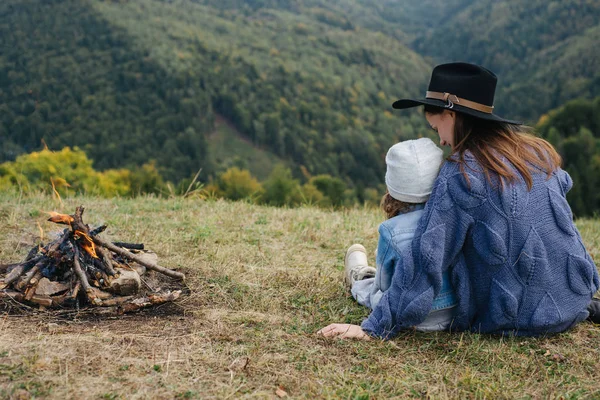 Όμορφη νεαρή μητέρα παίζει με την κόρη κοντά στη φωτιά σε βουνά σε άγριο Εθνικό Πάρκο δάσος. Η οικογένεια των ταξιδευτής χαλαρώνει μετά την ορειβασία. Καυκάσια γυναίκα με μωρό στα βουνά — Φωτογραφία Αρχείου