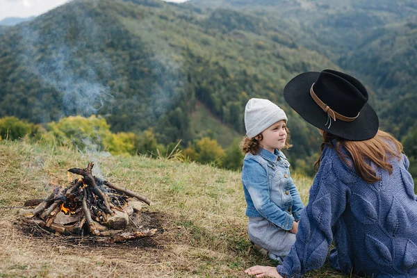 Μια νεαρή μητέρα και η όμορφη κόρη της κάθονται κοντά στη φωτιά σε βουνά σε άγριο Εθνικό Πάρκο δάσος. Η οικογένεια των ταξιδευτής χαλαρώνει μετά την ορειβασία. Καυκάσια γυναίκα με μωρό στα βουνά — Φωτογραφία Αρχείου