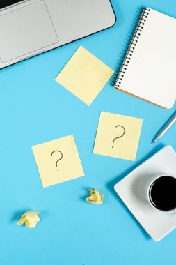 Yapışkan notlardaki soru işareti, defter, fincan kahve, dizüstü bilgisayar ve mavi arka plandaki kalem. Faq konsepti. Müşterilerle çalışmak. İşte sorunlar var. Düz konum, üst görünüm, kopyalama alanı