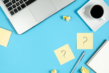 Sorular, kararlar. Yapışkan notlardaki soru işareti, defter, fincan kahve, dizüstü bilgisayar ve mavi arka plandaki kalem. Faq konsepti. Müşterilerle çalışmak. İşte sorunlar var. Düz konum, üst görünüm, kopyalama alanı