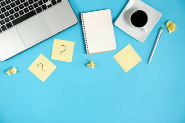 Sorular, kararlar. Yapışkan notlardaki soru işareti, defter, fincan kahve, dizüstü bilgisayar ve mavi arka plandaki kalem. Faq konsepti. Müşterilerle çalışmak. İşte sorunlar var. Düz konum, üst görünüm, kopyalama alanı