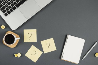 Sorular, kararlar. Yapışkan notlardaki soru işareti, defter, fincan kahve, dizüstü bilgisayar ve gri arka plandaki kalem. Faq konsepti. Müşterilerle çalışmak. İşte sorunlar var. Düz konum, üst görünüm, kopyalama alanı