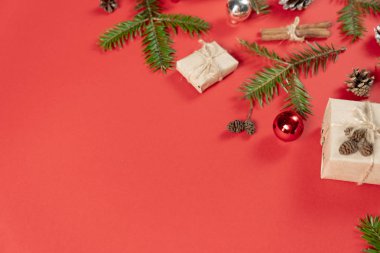 Noel ya da kış kompozisyonu. El yapımı hediye kutuları, köknar ağacı dallarından yapılmış el yapımı kağıt, çam ağacı ve tarçınlı pastel kırmızısı arka planda. Düz konum, üst görünüm, kopyalama alanı