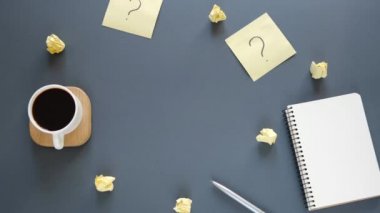 Kadın eli üzerinde soru işareti olan yapışkan notları kahve, kalem ve defterin yanındaki gri masaya koyar. Faq konsepti. Müşterilerle çalışmak. İşte sorunlar var. Düz konum, üst görünüm, kopyalama alanı