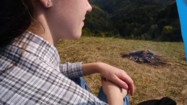 Kamp yapan kadının, kamp ateşinin yanında oturması, dağların manzarası, güzel ve ilham verici kamp yeri, yaşam tarzları.