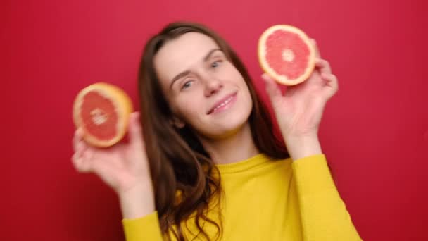 面白い漫画面白いユーモラスな女性の肖像画は 新鮮なグレープフルーツのスライスで遊んで 面白い若い女の子は喜んでカメラを見て柑橘系の果物を保持し 赤い壁の背景に孤立 — ストック動画
