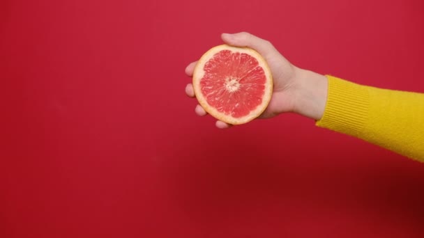 靠近女性的手捏着新鲜的切碎柚子 柑橘类果汁从纸浆和滴水中排出 在带有复制空间的红色工作室背景下隔离 — 图库视频影像