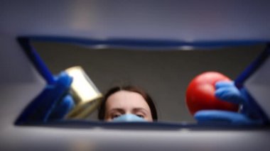 Koruyucu tıbbi maske ve eldiven takan esmer kadının alt görünüşü yiyeceği kutuya koyar. Coronavirus salgını sırasında evden ve sosyal mesafelere çalışmak için gıda dağıtım hizmetleri. Yardım kavramı