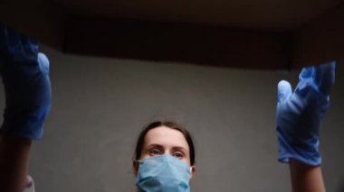 Tıbbi maske takan esmer kadın ve lateks eldivenlerin altından çekilen kutu çevrimiçi dükkandan dikkatlice açıldı. Konsept koronavirüs salgını karantinası, ev izolasyonu, sosyal uzaklık