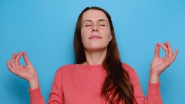 Güzel, çekici bir kadın yoga egzersizi yapıyor, kırmızı kazak giyiyor, hoş bir kız meditasyon yapıyor, mavi arka planın üzerinde duruyor, iç dengeyi hissediyor parmaklarını mudra hareketi yapıyor, stres konsepti yok.