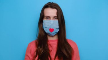 Coronavirus COVID-19 salgını sırasında hastanede çalışan hemşire ve tıbbi personele teşekkür etmek için göğsünde küçük bir kalp taşıyan bir maske takan sevimli genç bir kadın.