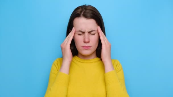 ストレスの多い不幸な若い女性の肖像頭痛の感情的なストレス救済を緩和し 疲れた神経の少女のマッサージ寺院 黄色のセーターを着て 青のスタジオの背景に隔離された — ストック動画