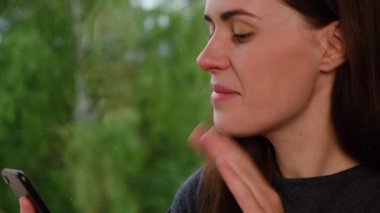 Neşeli esmer bir kadının telefon kulübesinde oturduğu pencerenin kenarında otururken görüntülü konuşma yaptığı bir video. Çevrimiçi uygulama, sosyal uzaklık, evden çalışma. Yeni normal kavram