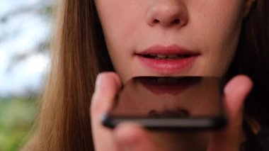 Telefonu elinde tutan genç kadına yakın çekim yap. Sanal dijital ses asistanını akıllı telefondan aktive et. Kız sesli mesaj kaydet.