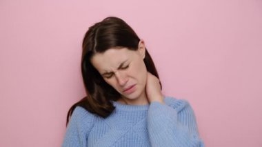 Üzgün genç bir kadın masaj yaparken boynu incindi, yorgun esmer kız omuz ağrısını hafifletmek için kaslarını ovdu, fibromiyalji konsepti, pembe stüdyo arka planında izole edildi.