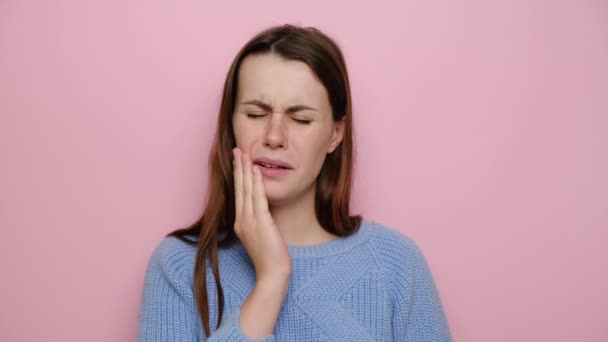 不幸な若い女性は頬に触れ 歯痛に苦しみ 少女はひどい突然の歯痛を経験し 歯科治療を必要とし ピンクのスタジオの背景に隔離されたセーターを着ています 医療保険の概念 — ストック動画