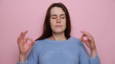 Yoga yapan neşeli genç bir kadın, süveter giyiyor, meditasyon yapan tatlı bir kız, pembe stüdyo arka planının başında dikiliyor iç dengeyi hissediyor parmaklarını mudra hareketi yapıyor, stres konsepti yok.